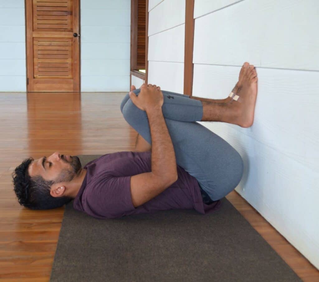 Man in gray leggings and a maroon shirt practicing a modification and variation for Legs Up The Wall Pose with his knees bent in Blue Osa's yoga shala in Costa Rica.