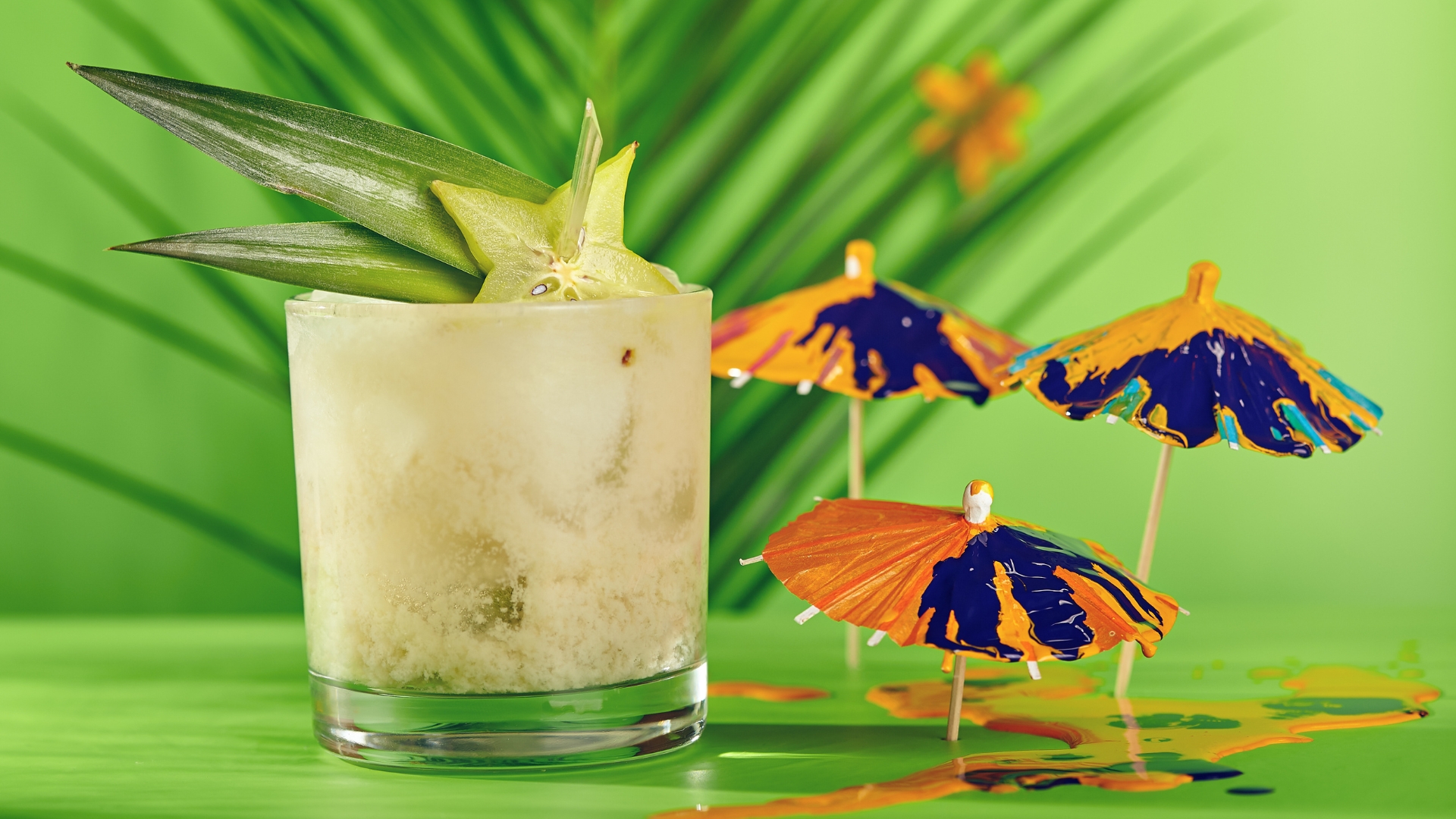 Exotic cocktail with a star fruit garnish and pineapple stems with a green background and orange and purple cocktail umbrellas.