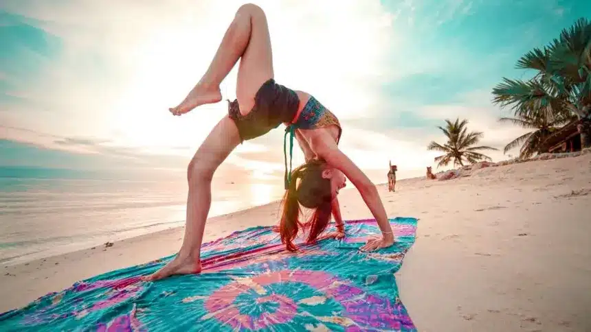 woman on the beach, on a sarong, in a wheel yoga pose with the sun in the background koh phangan thailand
