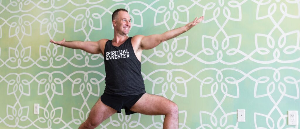 practice the 30-day yoga challenge at home | Yogi Aaron in Warrior 2 yoga pose wearing a spiritual ganster tank top