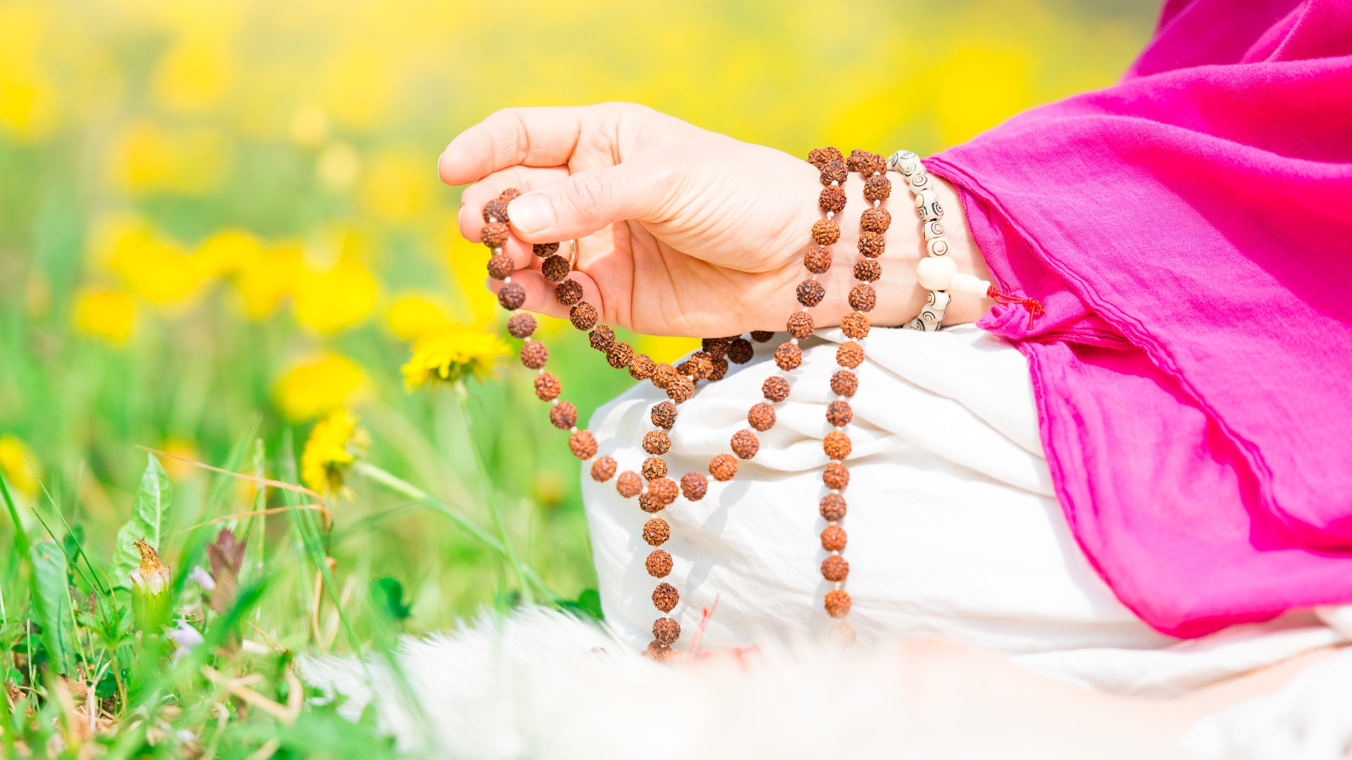Woman sitting in a meditative position holding mala beads in her hand.