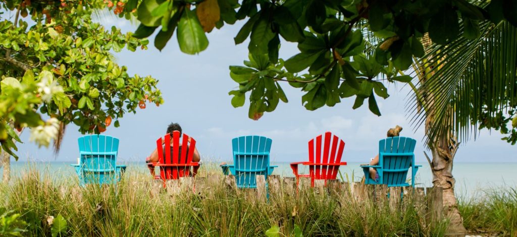 Two people sitting red and blue adirondack chairs facing the turquoise golfo dulce at Blue Osa in Costa Rica.