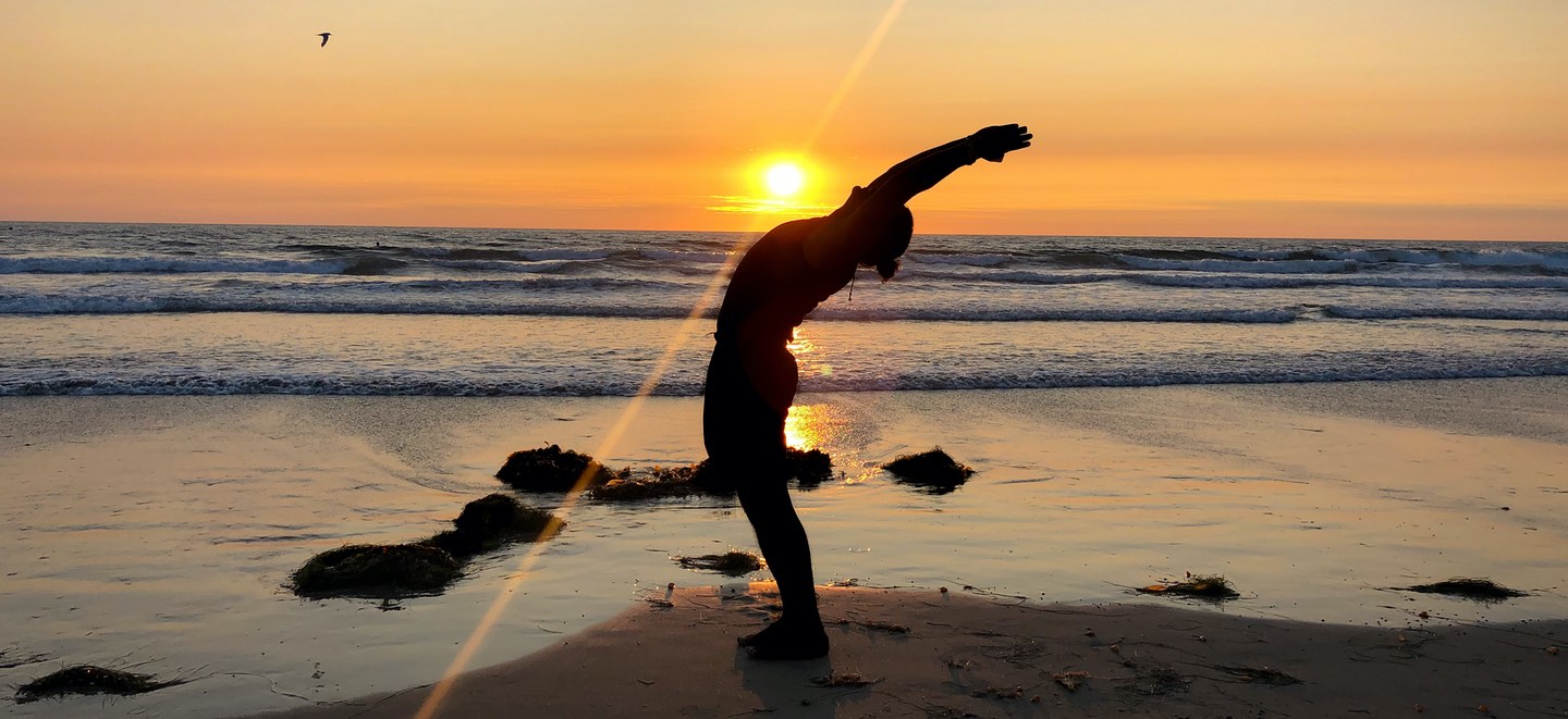 Silhouette of a man doing a standing back bend in front of a setting sun on the beach in Costa Rica.