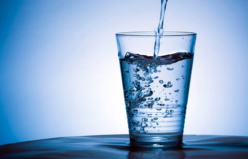 Blue tinted image of water being poured into a clear glass of water.