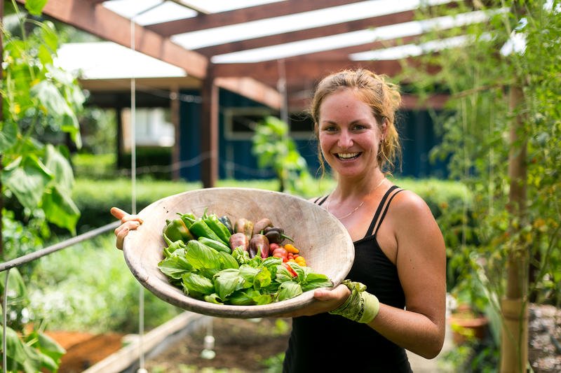 Woman standing with a giant wooden bowl full of fresh veggies picked from the 