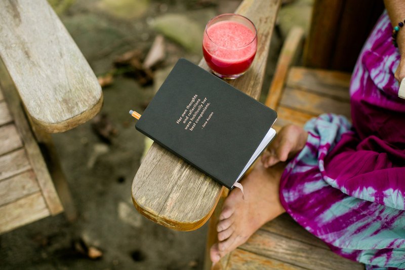 Image of a woman sitting on a chair with a pink smoothie and a book that reads "Her own thoughts and reflections were habitually her best companions" by Jane Austin