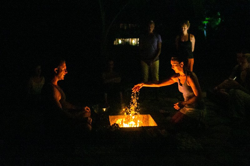 Yoga students participating in a fire ritual at night throwing sand in a fire at Blue Osa yoga retreat center in Costa Rica. 