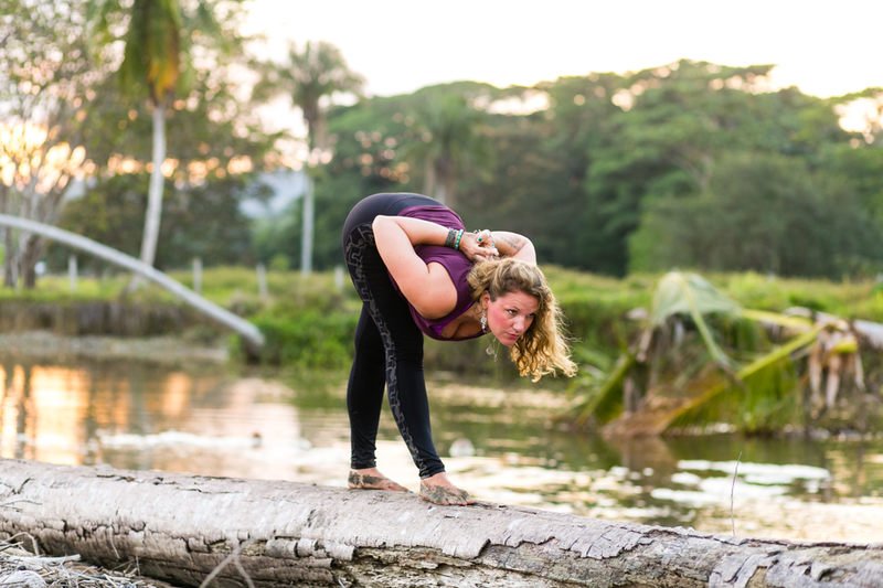 Woman in a purple shirt and black leggings practicing pyramid pose on a log in Costa Rica. 