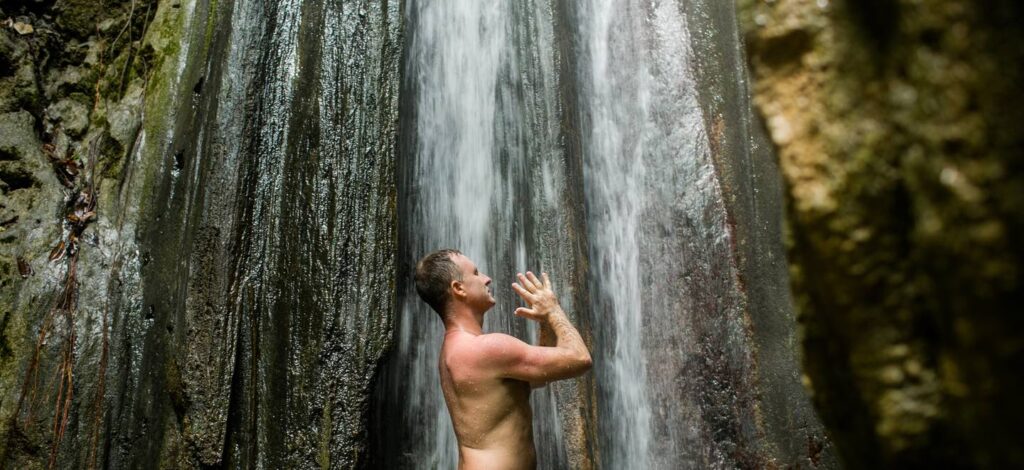Yogi Aaron standing under a waterfall with his hands in prayer position in Costa Rica. 