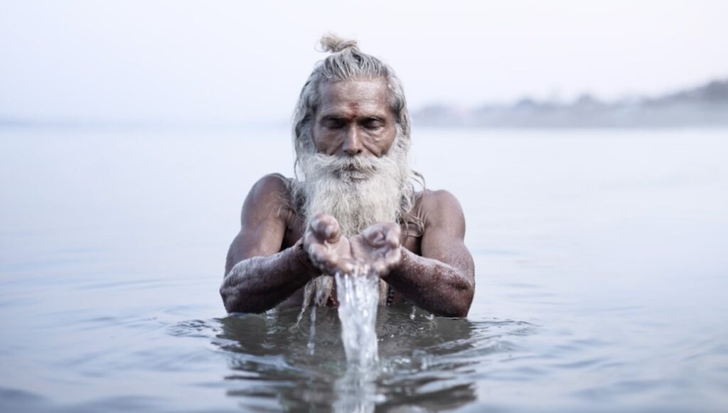 Indian man holding out his hands spilling water while standing in a river. 