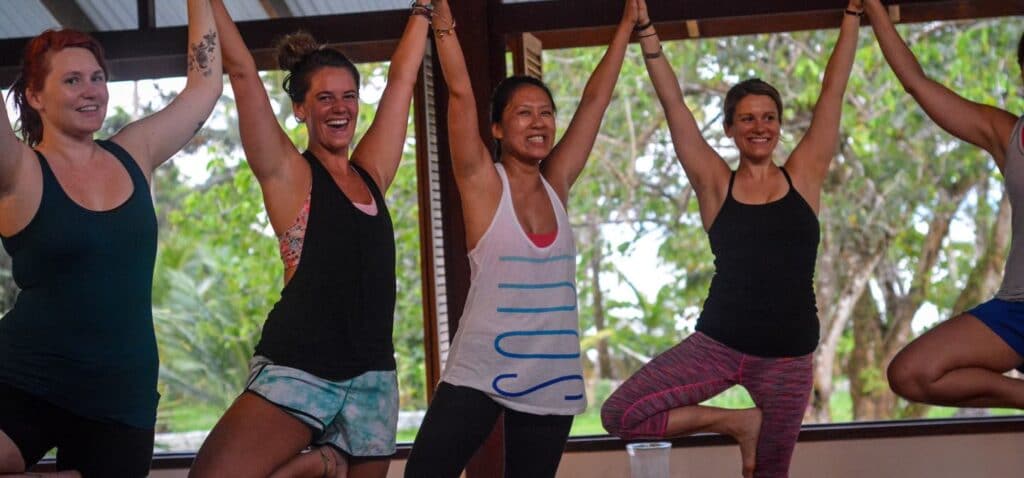 Yoga students standing in tree pose holding hands above their heads in Blue Osa's yoga shala in Costa Rica.
