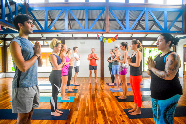 Yoga students lined up facing each other standing with feet together and hands in prayer pose in Blue Osa's yoga shala in Costa Rica. 