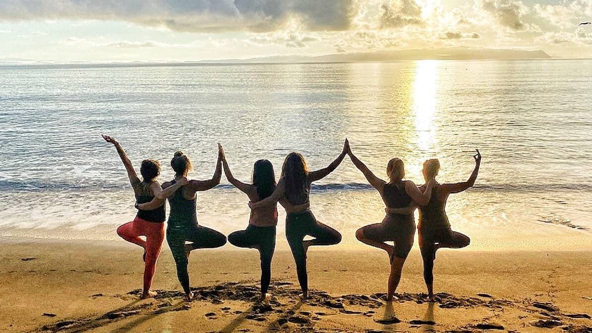 Group of women on the beach in Tree Pose doing partner yoga
