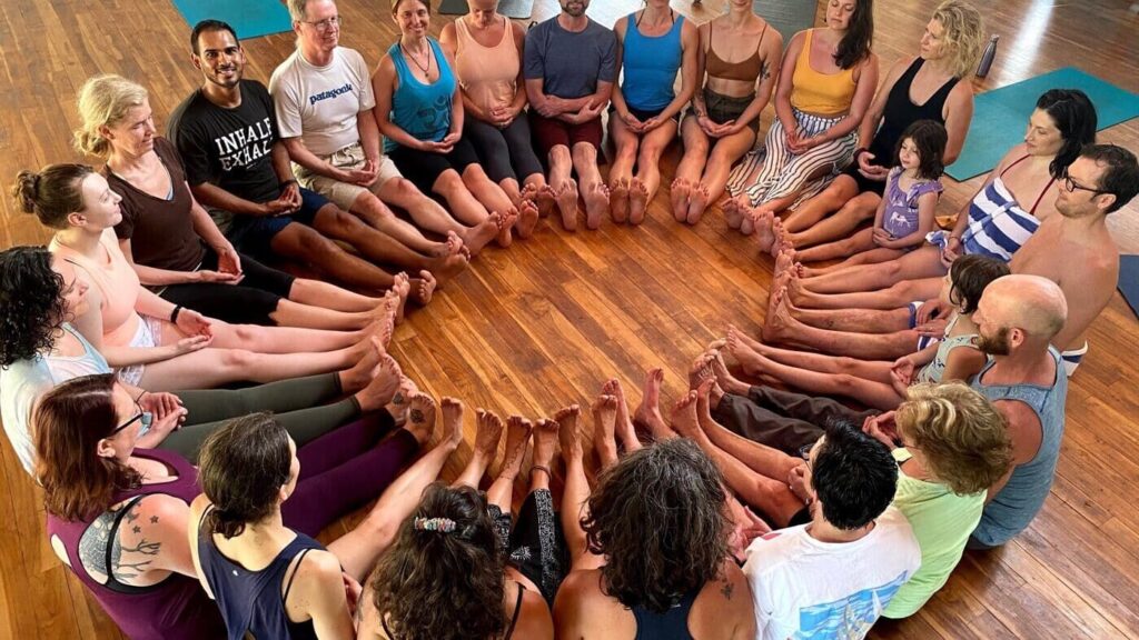 Yoga students sitting in a circle with their legs in front of them and sides of their feet touching in Blue Osa's yoga shala in Costa Rica.