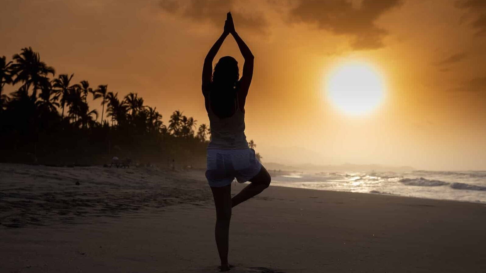 Woman on the beach in tree pose at sunset