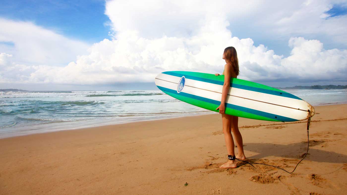 Surfer girl standing on beach with board looking at ocean