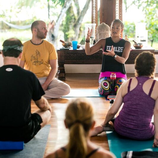 Yoga teacher talking to a room full of yoga students in Blue Osa's yoga shala in Costa Rica. 