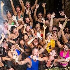 Smiling yoga students standing under a waterfall in Costa Rica with their hands up in the air.