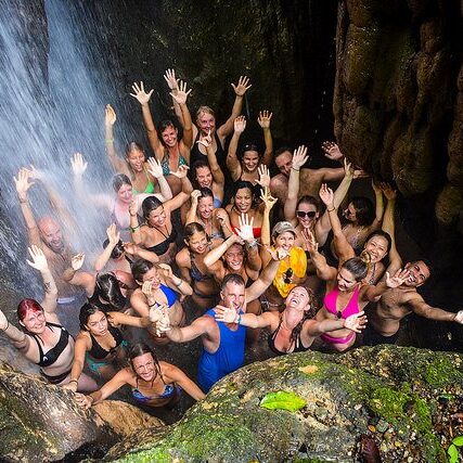 Group of yoga students standing under a waterfall with Yogi Aaron with their hands up in the air in Costa Rica.