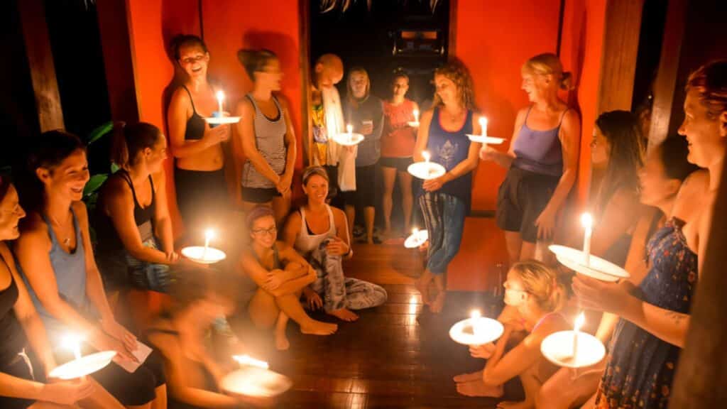 Group of yoga students standing around a circle holding candles during a meditation as part of their yoga teacher training at Blue Osa in Costa Rica.