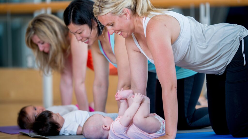 Three moms in all four position on their hands and knees looking over their babies on yoga mats. 