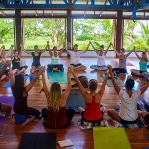Yoga students sitting in a circle holding hands raised above their heads in Blue Osa's Yoga Shala in Costa Rica.