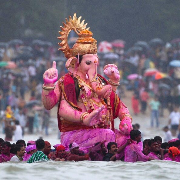 Bright pink Ganesh statue being held up by a bunch of Hindu men at a Hindu celebration. 