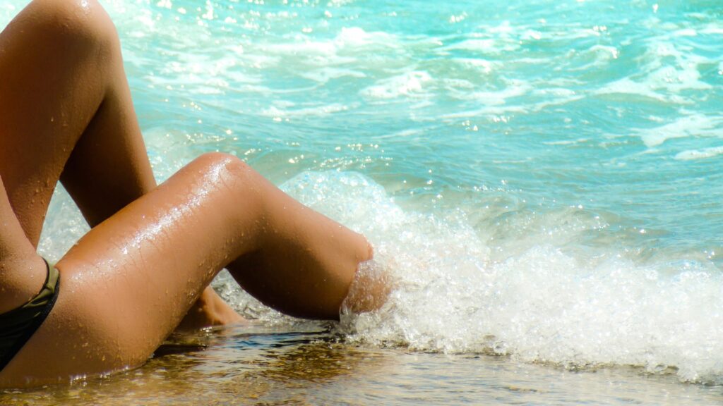 Woman sitting on the ocean's edge with a wave splashing over her legs. 