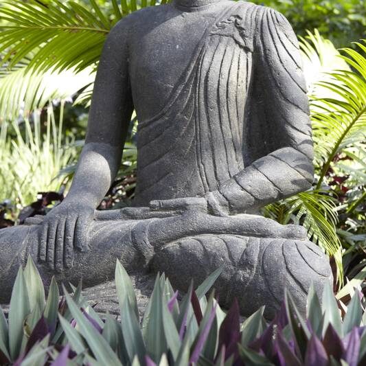 the torso of a buddah statue surrounded by gardens. 