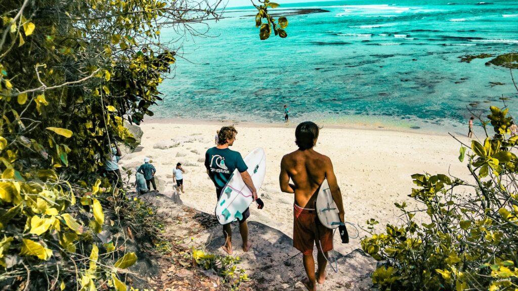 Two surfers walking towards the turquoise ocean on Dominical Beach in Costa Rica. 
