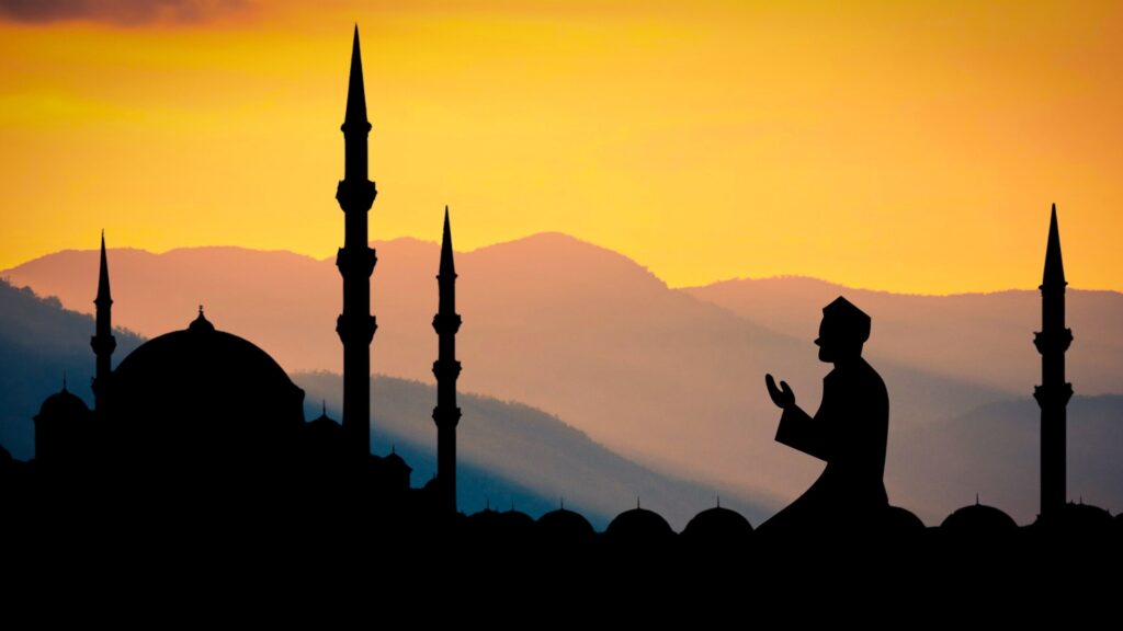 Silhouette of an Islam praying with a sunset and mountains in the background. 