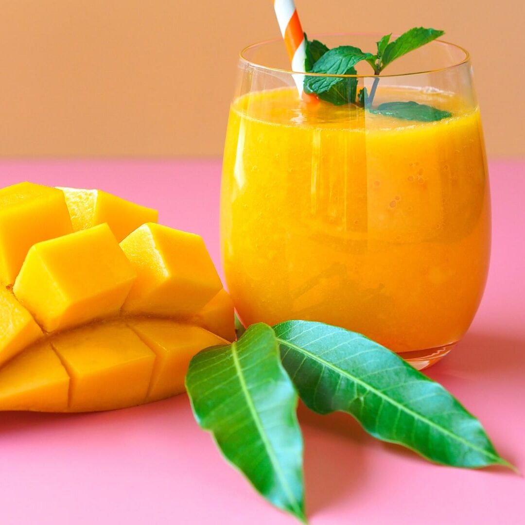 Mango smoothie in a glass next to cubed mangos.