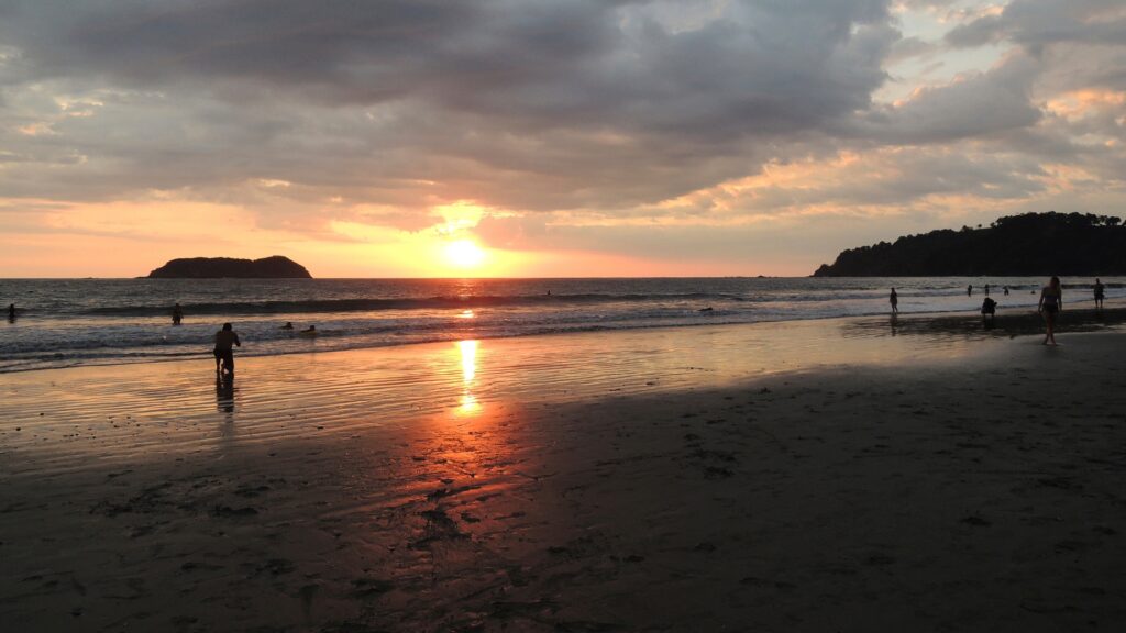 A setting sun over the ocean with beach goers on Playa Espadilla in Costa Rica.