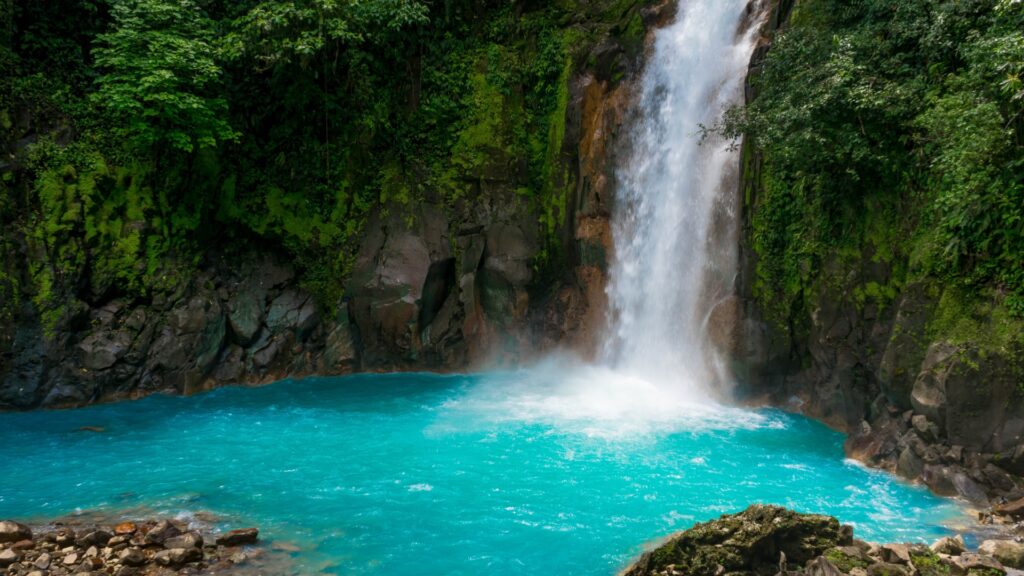 A waterfall cascading into a lagoon of turquoise blue water with greenery surround the waterfall in Costa Rica. 