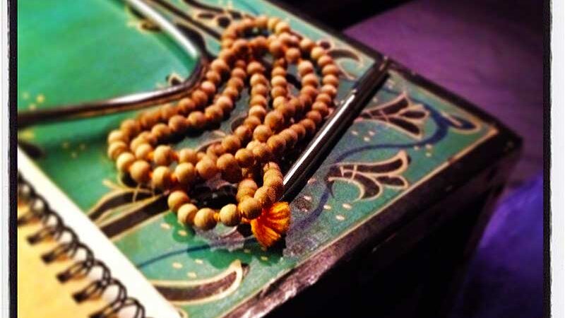 Mala beads with an orange tassel sitting on a green notebook.