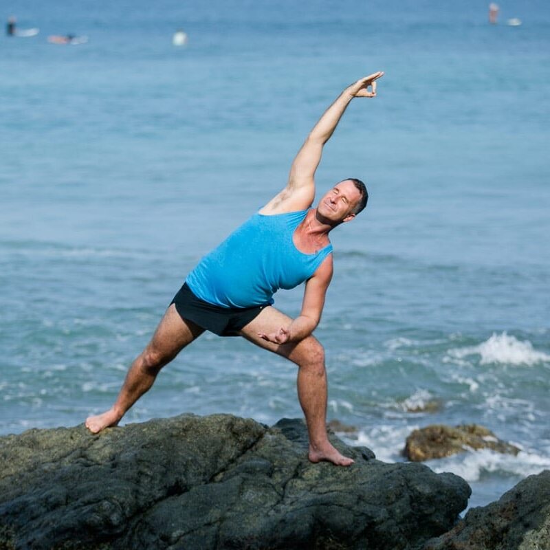 Yogi Aaron practicing a side lunge yoga pose on a rock in front of the ocean in Costa Rica. 