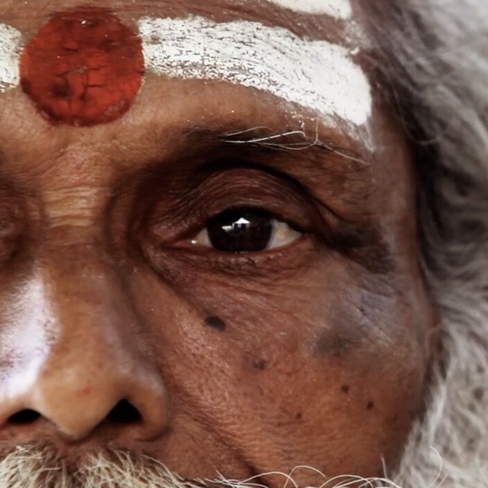 Elderly Indian man with white stripes and a red circle painted on his head. 