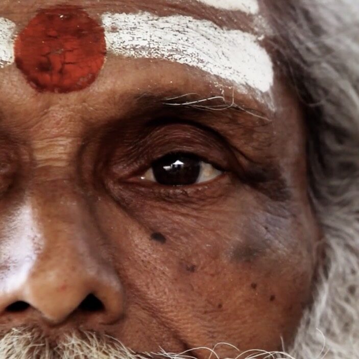 Elderly Indian man with white stripes and a red circle painted on his head.