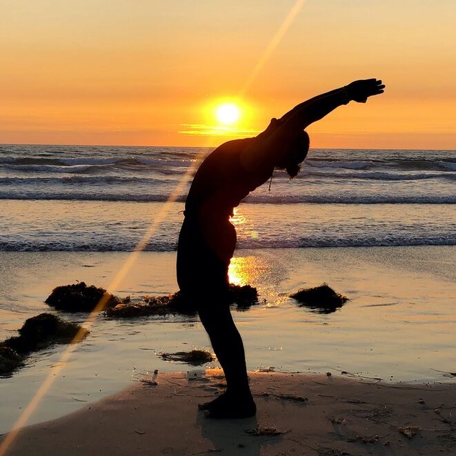 Silhouette of a man doing a standing back bend in front of a setting sun on the beach in Costa Rica.