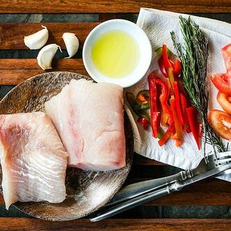 Plate of white fish and colorful vegetables on a wooden table with silverware. 