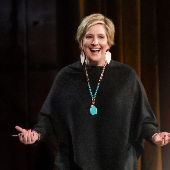 Brene Brown presenting on stage in a black sweater and turquoise necklace. 