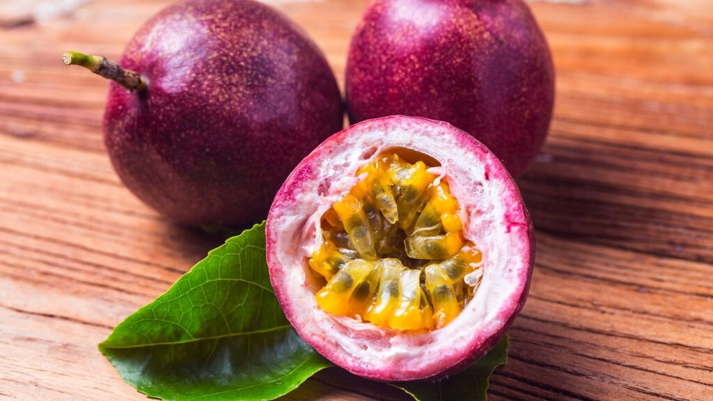 A ripe purple passion fruit cut open showing the yellow pulp and sees inside.
