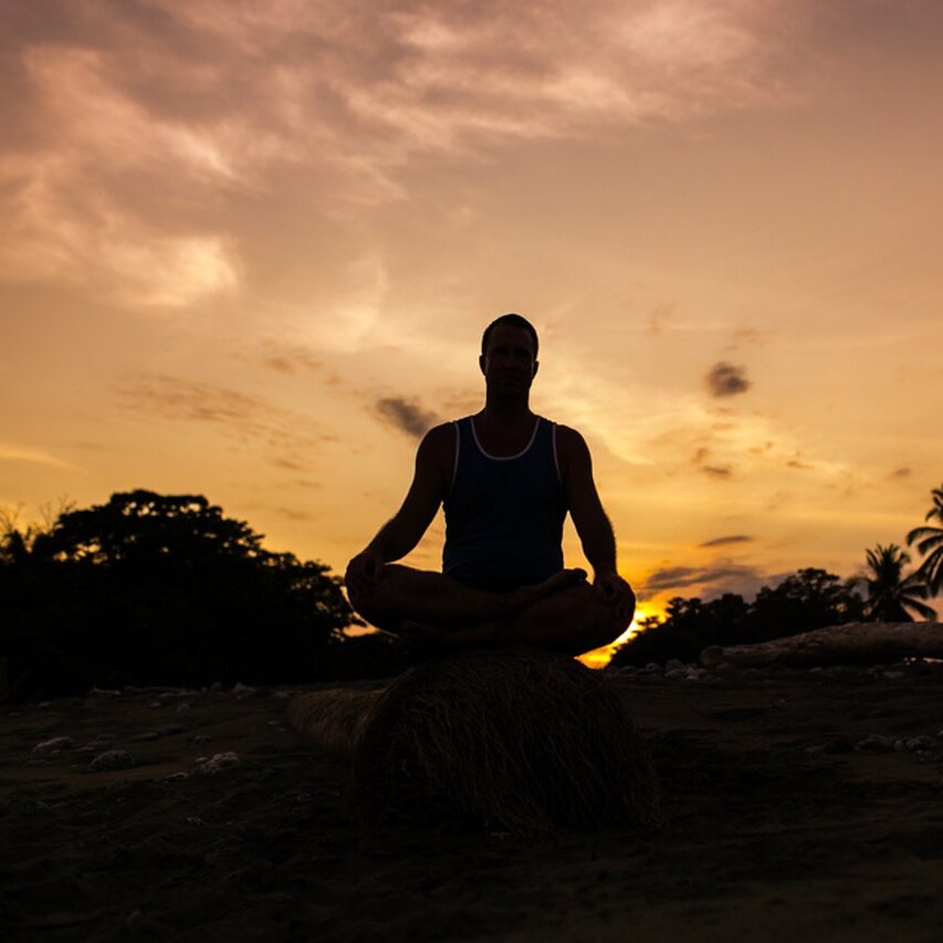 Silhouette of Yogi Aaron sitting in meditation with a sunset behind him.