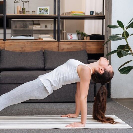 Woman in her home in front of her couch practicing a reversed plank.