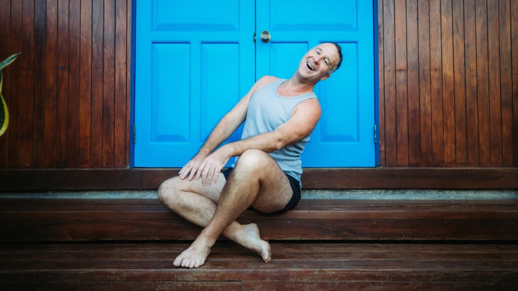 Yogi Aaron sitting on dark wooden steps in front of a bright blue door outside Blue Osa's spa in Costa Rica. 