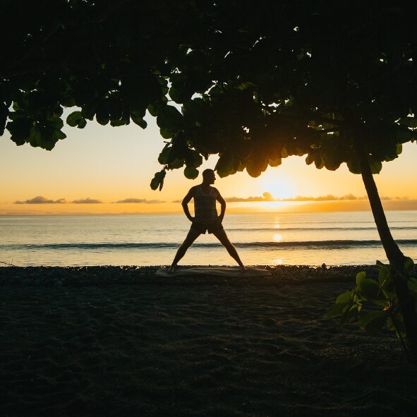 Silhoutte of Yogi Aaron in a wide legged standing position on the beach in front of Blue Osa in Costa Rica.