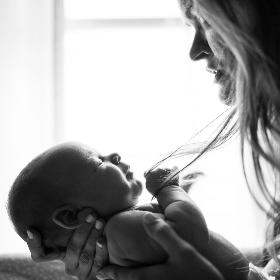 Black and white image of a mother with a stressed look on her face looking at her baby that she's holding in her hands. 