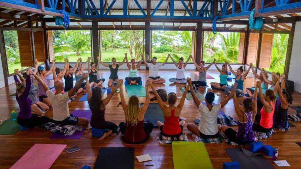 Yoga students sitting in a circle holding hands raised above their heads in Blue Osa's open aired yoga shala in Costa Rica. 