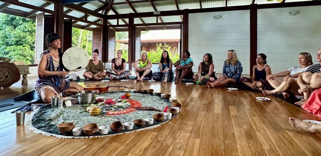 group of people in a circle singin and chanting, a woman playing a drum, in a yoga studio at blue osa in costa rica. Blue Osa yoga retreat Costa Rica transformative practice shadow work training