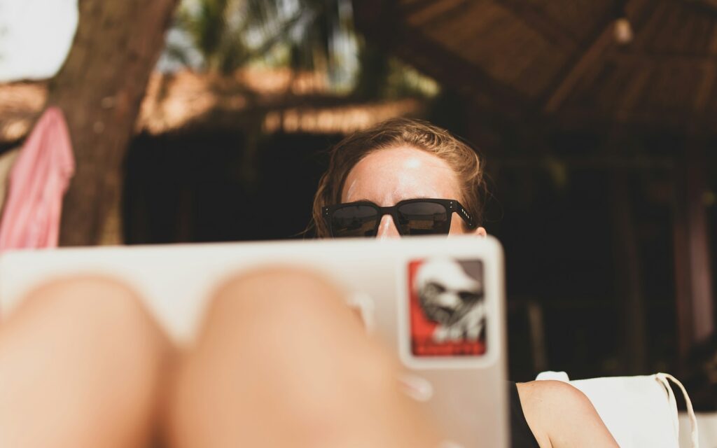 woman wearing black framed sunglasses working vacation laptop poolside